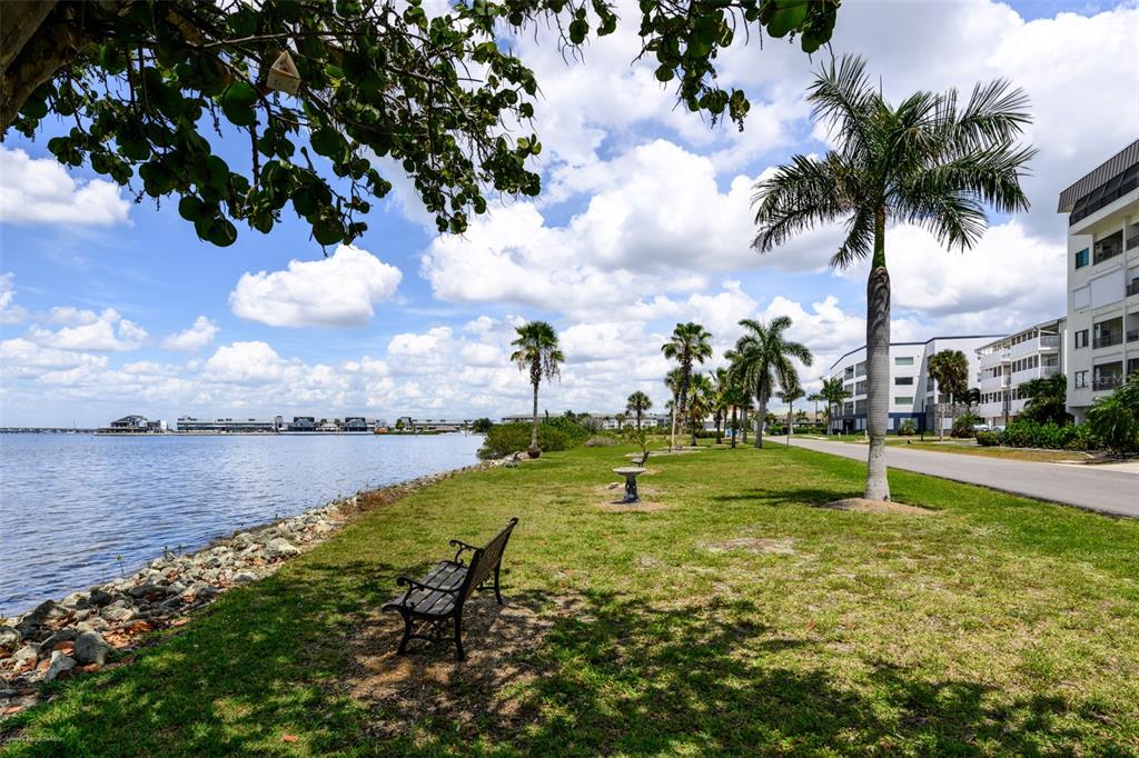 A park-like waterfront area features a bench, palm trees, and a nearby apartment building — 1477 PARK BEACH CIRCLE UNIT 33, PUNTA GORDA, FL