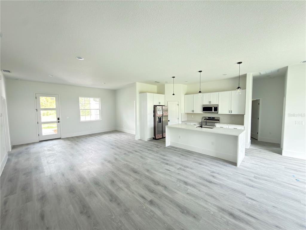 An open-concept kitchen and living area features white cabinetry, a kitchen island, and light-colored flooring — 3679 SW 129TH PLACE, OCALA, FL