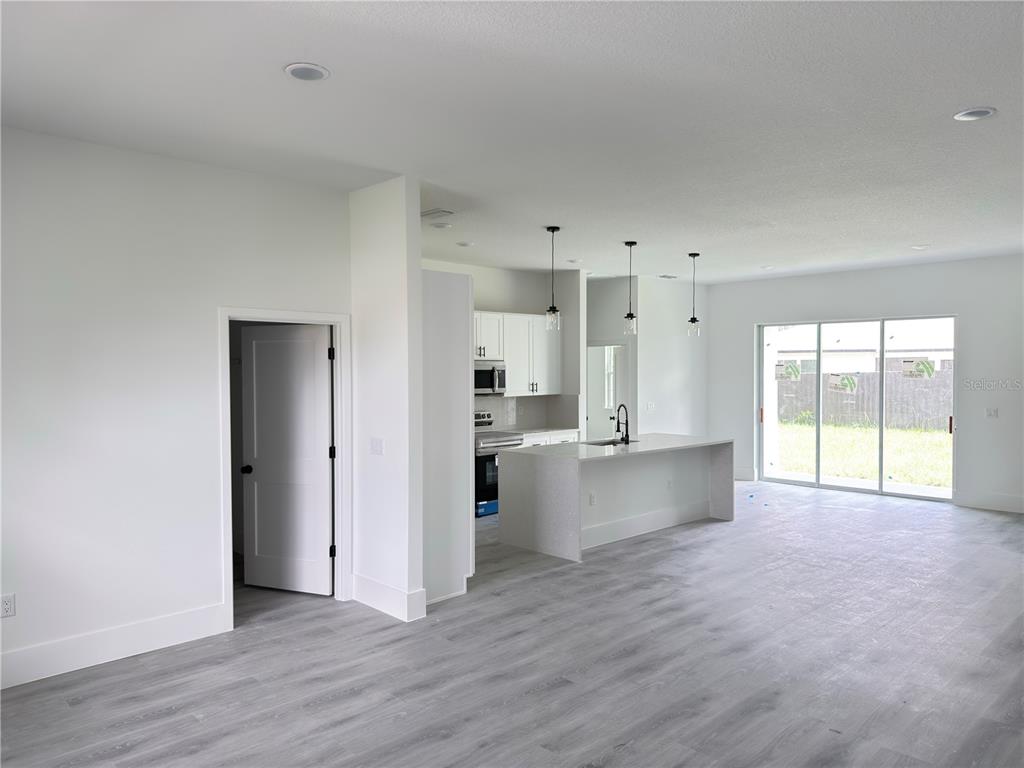An open-concept kitchen and living area features white cabinets, a quartz island, and gray flooring — 3679 SW 129TH PLACE, OCALA, FL