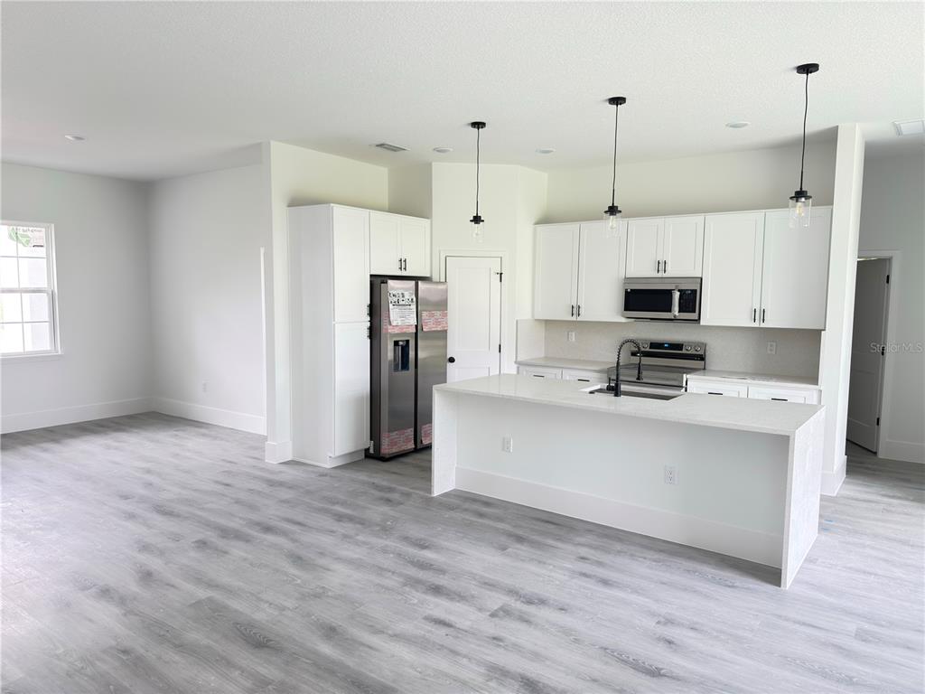 A modern kitchen features white cabinets, stainless steel appliances, a quartz island, and gray flooring — 3679 SW 129TH PLACE, OCALA, FL