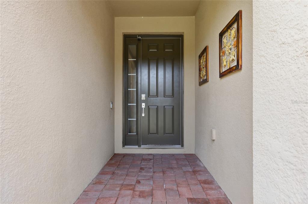 A dark brown front door with a side window sits at the end of a porch — 3865 BOWFIN TRAIL, KISSIMMEE, FL
