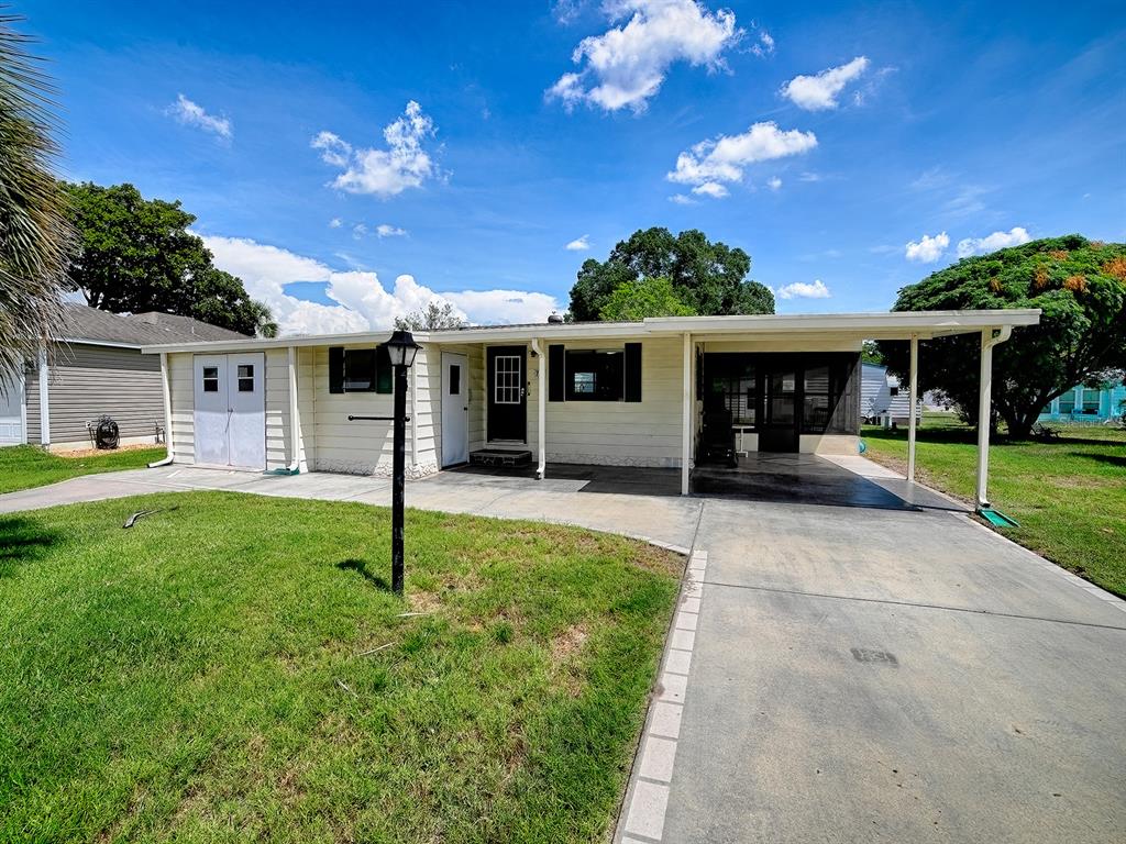 A single-story house with light siding, a carport, and a concrete driveway under a blue sky — 721 SHARON DRIVE, LADY LAKE, FL