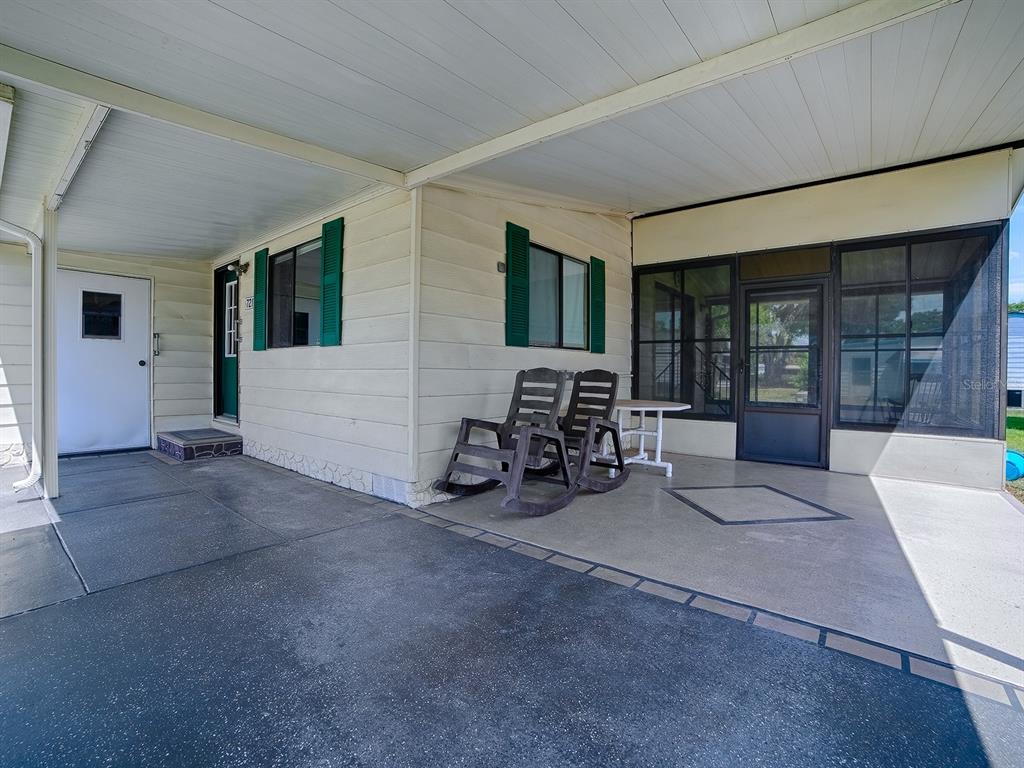 A covered concrete patio features two rocking chairs, a small table, and a screened enclosure — 721 SHARON DRIVE, LADY LAKE, FL