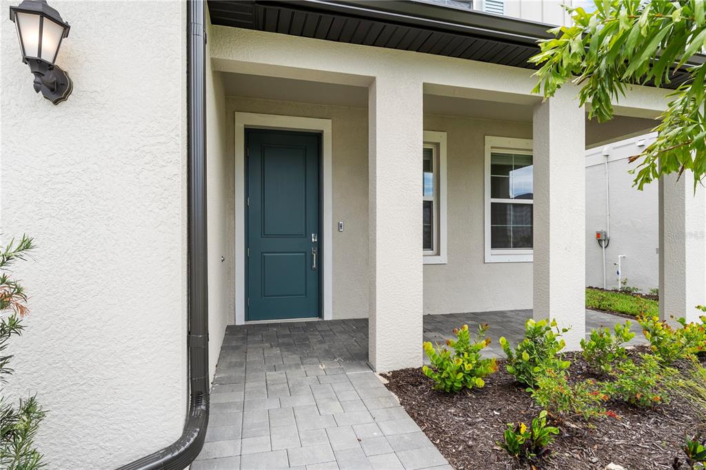 A teal front door is set within a covered entryway with stone pavers and landscaping — 45012 PIPEVINE CIRCLE, PUNTA GORDA, FL