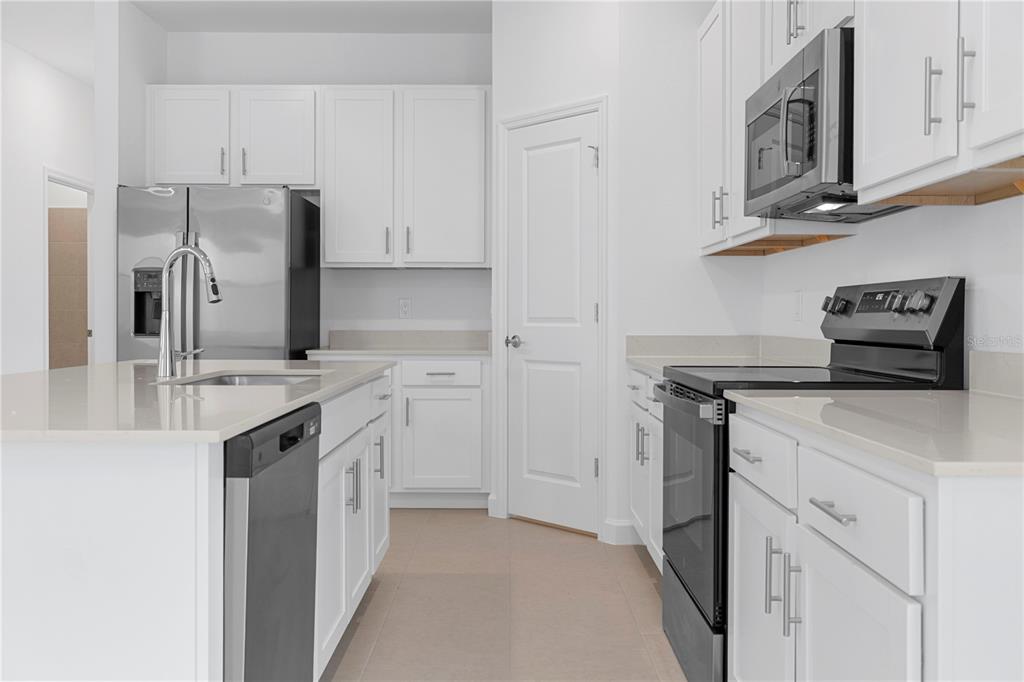 A modern kitchen features white cabinets, stainless steel appliances, and a central island with seating — 45012 PIPEVINE CIRCLE, PUNTA GORDA, FL