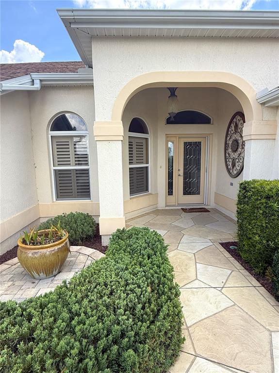 An exterior view of a home entrance with a stone walkway, arched porch, and landscaping — 754 CHAPMAN LOOP, THE VILLAGES, FL