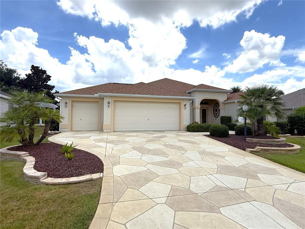 A single-story house with a three-car garage and a decorative stone-patterned concrete driveway — 754 CHAPMAN LOOP, THE VILLAGES, FL