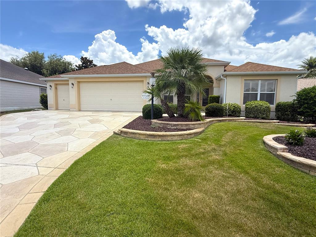 A single-story house with a beige exterior, a three-car garage, and a landscaped front yard — 754 CHAPMAN LOOP, THE VILLAGES, FL
