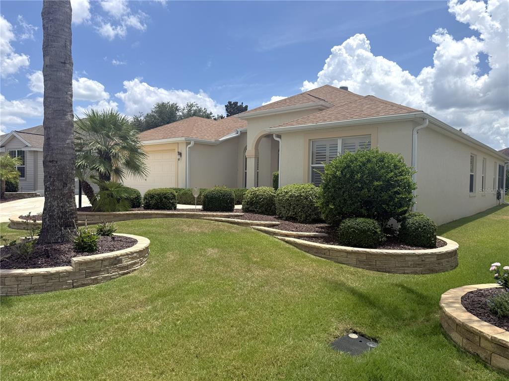 A single-story house with a tan stucco exterior, a shingled roof, and tiered stone landscaping — 754 CHAPMAN LOOP, THE VILLAGES, FL
