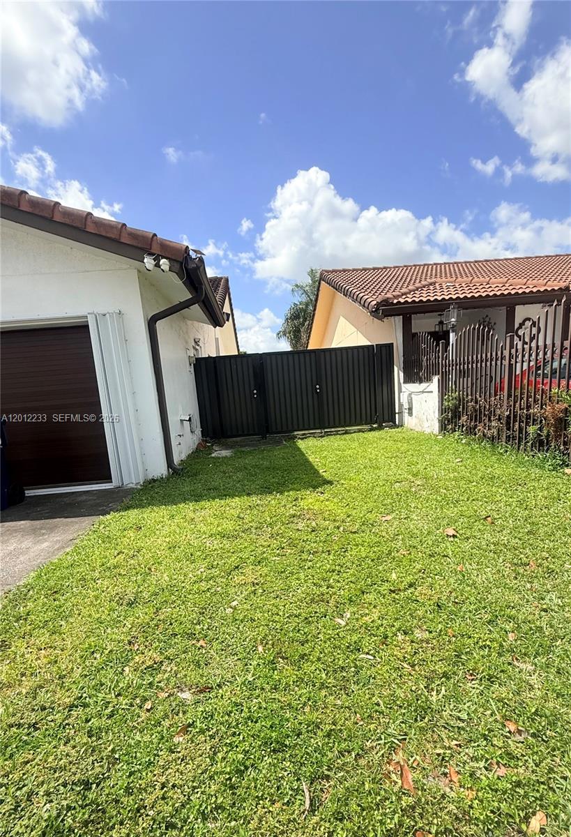 A grassy yard sits between two houses with a black metal gate in the background — MIAMI, FL