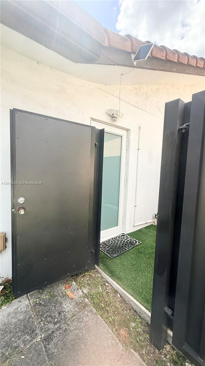 A black metal gate opens to a white door with a small solar panel above — MIAMI, FL