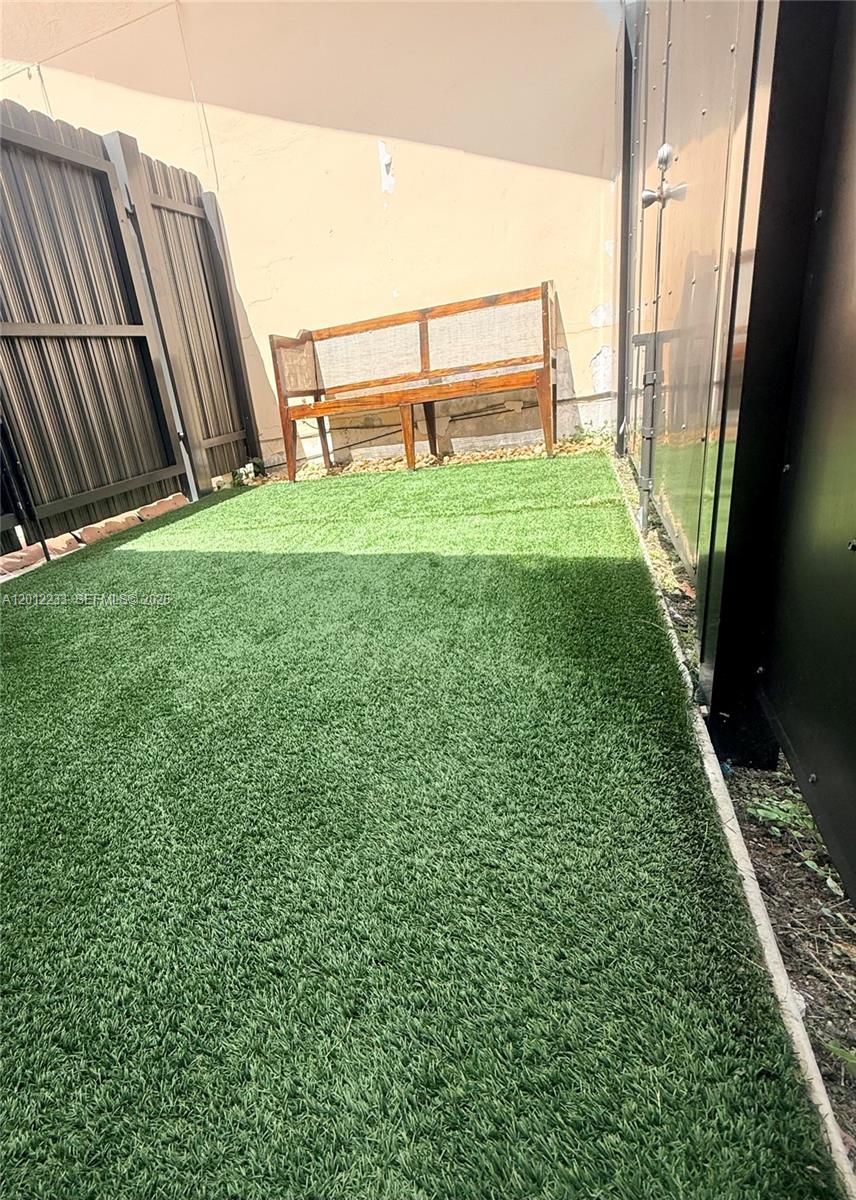 A small outdoor patio features artificial turf, a wooden bench, and privacy fencing — MIAMI, FL
