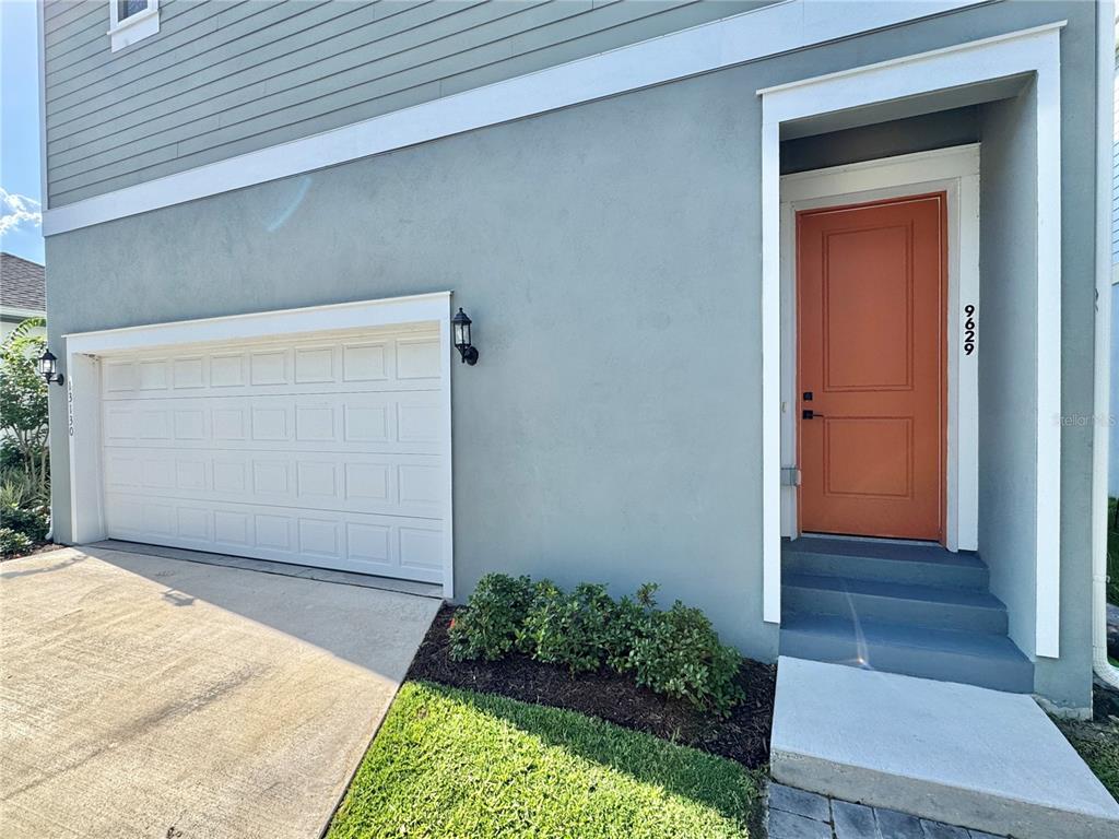 The exterior of a house features a white garage door, a light blue wall, and an orange front door — 9629 SARAMAGO ALLEY, ORLANDO, FL
