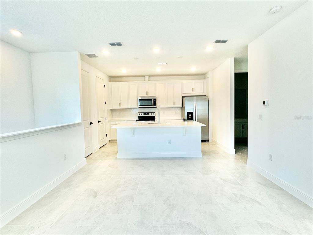 A modern kitchen features white cabinetry, stainless steel appliances, a center island, and tile flooring — 9629 SARAMAGO ALLEY, ORLANDO, FL