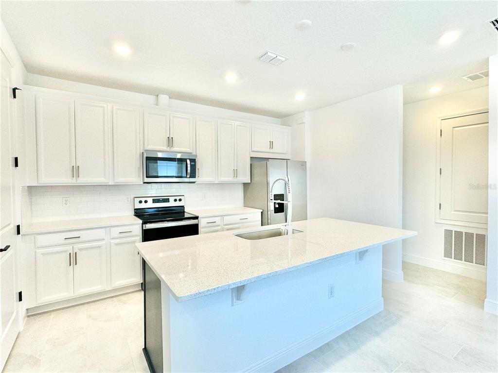 A modern kitchen features white cabinetry, stainless steel appliances, and a large central island — 9629 SARAMAGO ALLEY, ORLANDO, FL