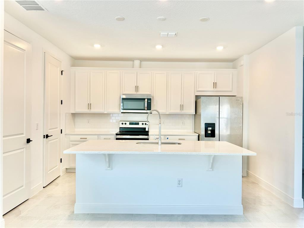 A modern kitchen features white cabinetry, stainless steel appliances, and a large central island — 9629 SARAMAGO ALLEY, ORLANDO, FL