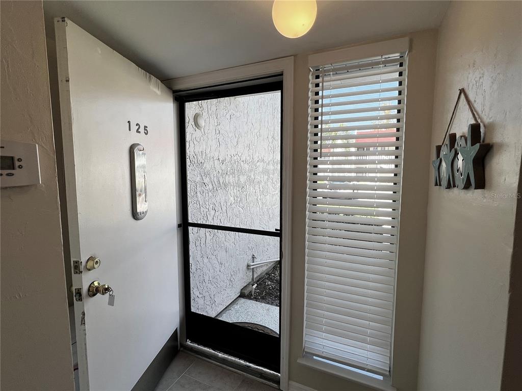 An entryway features a white door numbered 125, a screen door, and a window with blinds — 1801 GULF DRIVE N UNIT 125, BRADENTON BEACH, FL