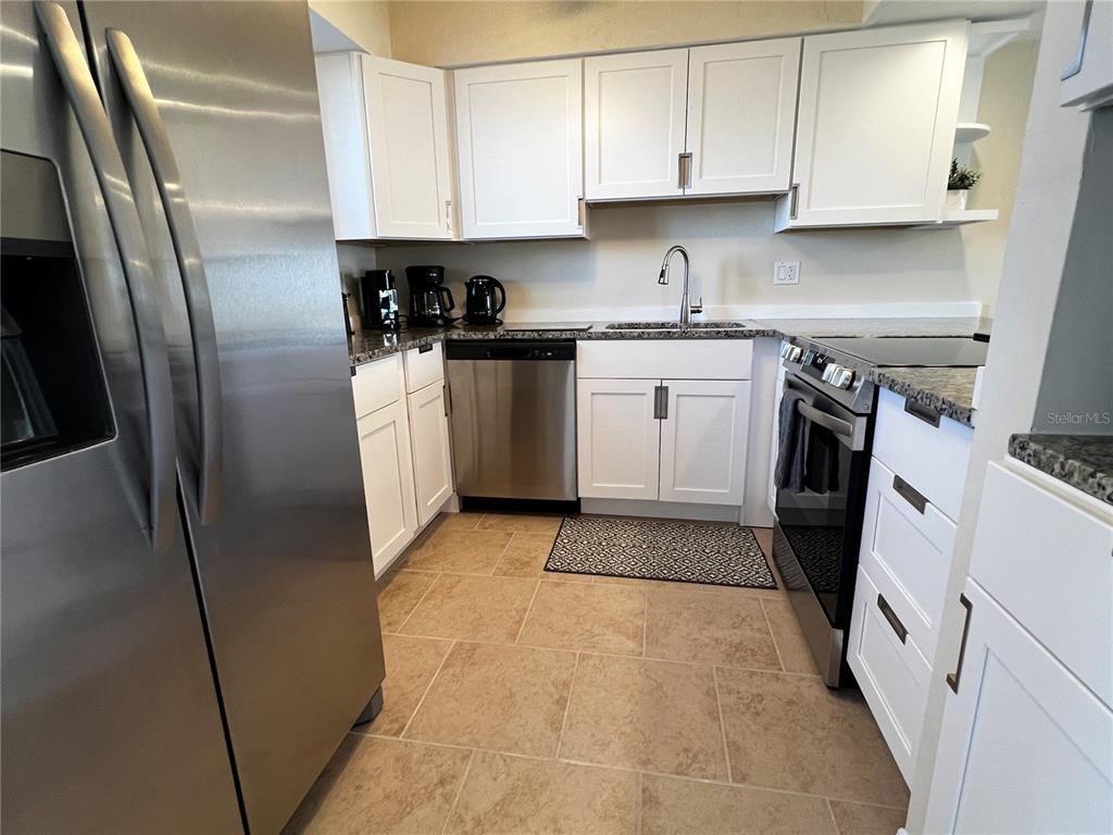 A kitchen features white cabinets, stainless steel appliances, and tan tile flooring — 1801 GULF DRIVE N UNIT 125, BRADENTON BEACH, FL