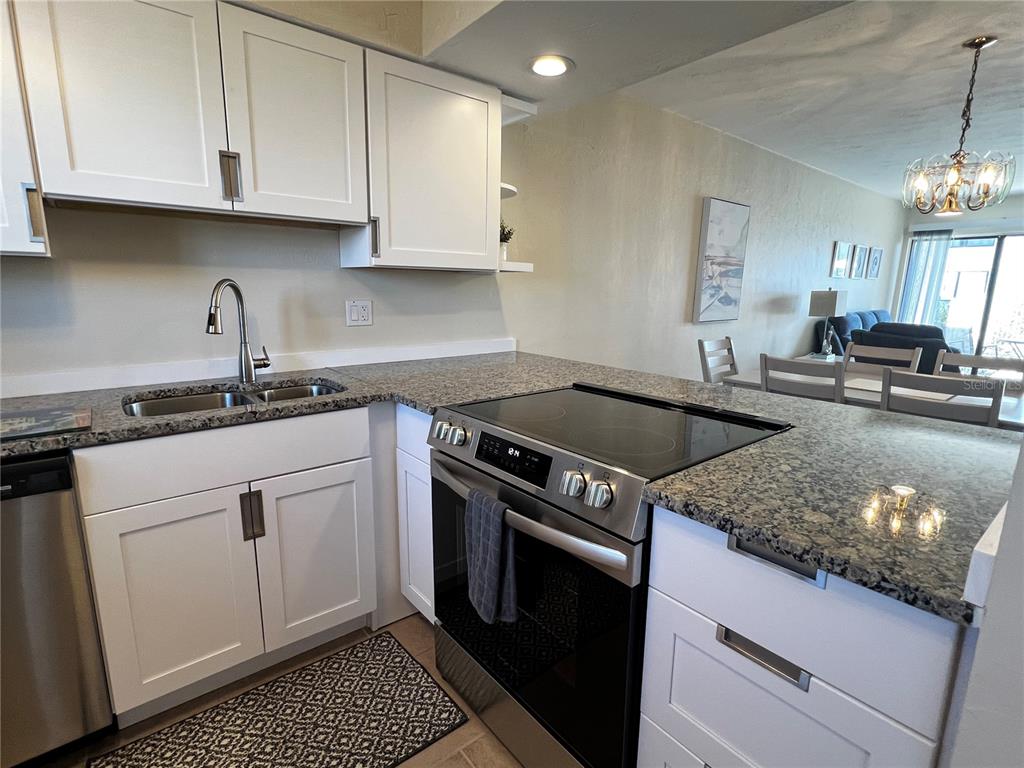 A kitchen features white cabinets, granite countertops, stainless steel appliances, and an open floor plan — 1801 GULF DRIVE N UNIT 125, BRADENTON BEACH, FL