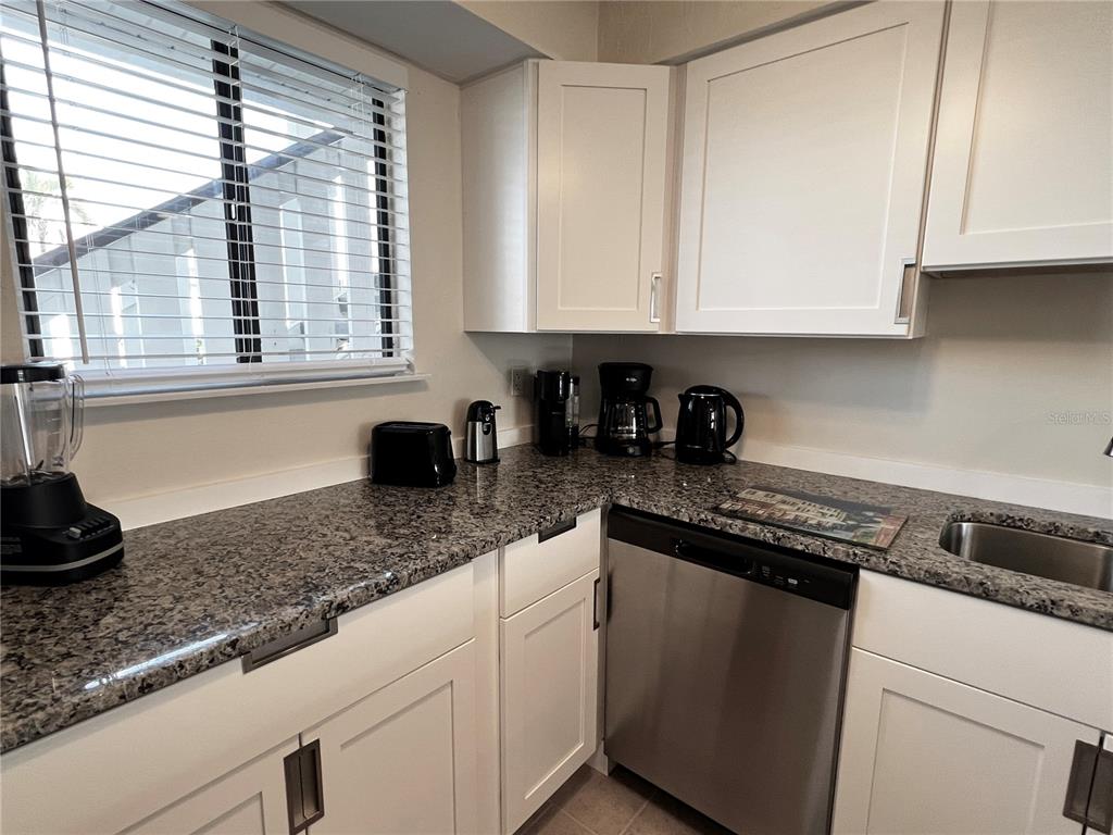 A kitchen features white cabinets, granite countertops, a stainless steel dishwasher, and a window — 1801 GULF DRIVE N UNIT 125, BRADENTON BEACH, FL