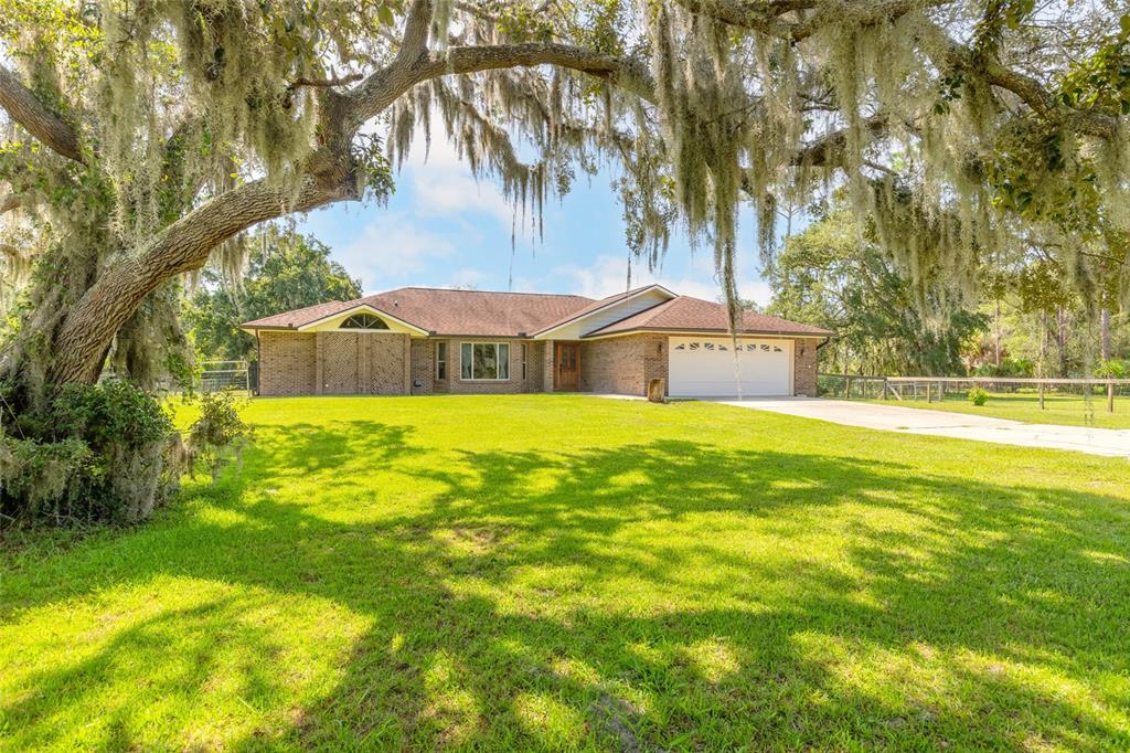 A single-story brick house with a two-car garage sits on a grassy lot with trees — 1389 WILLIAMS ROAD, NEW SMYRNA BEACH, FL