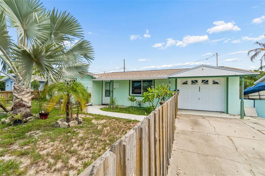 A light green single-story house features a white garage door and a wooden fence — 1056 TAMARAC DRIVE, HOLIDAY, FL