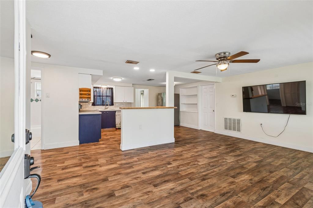 An open-concept living room and kitchen featuring wood-look flooring and a wall-mounted television — 1056 TAMARAC DRIVE, HOLIDAY, FL