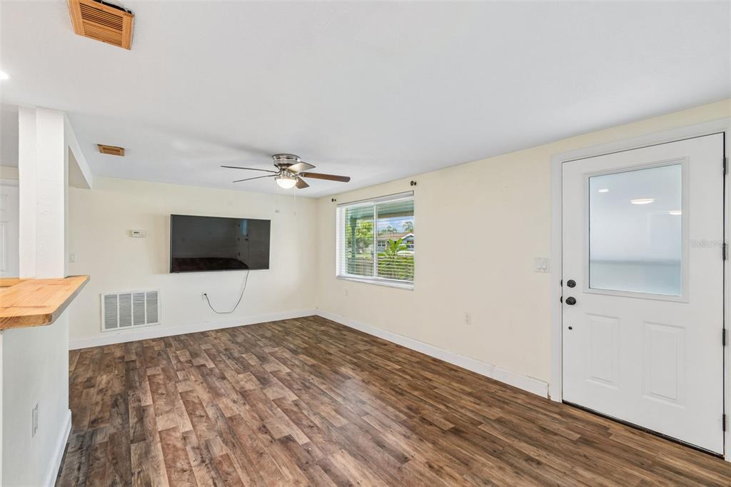 A living room with wood-look flooring, a ceiling fan, a wall-mounted television, and an exterior door — 1056 TAMARAC DRIVE, HOLIDAY, FL