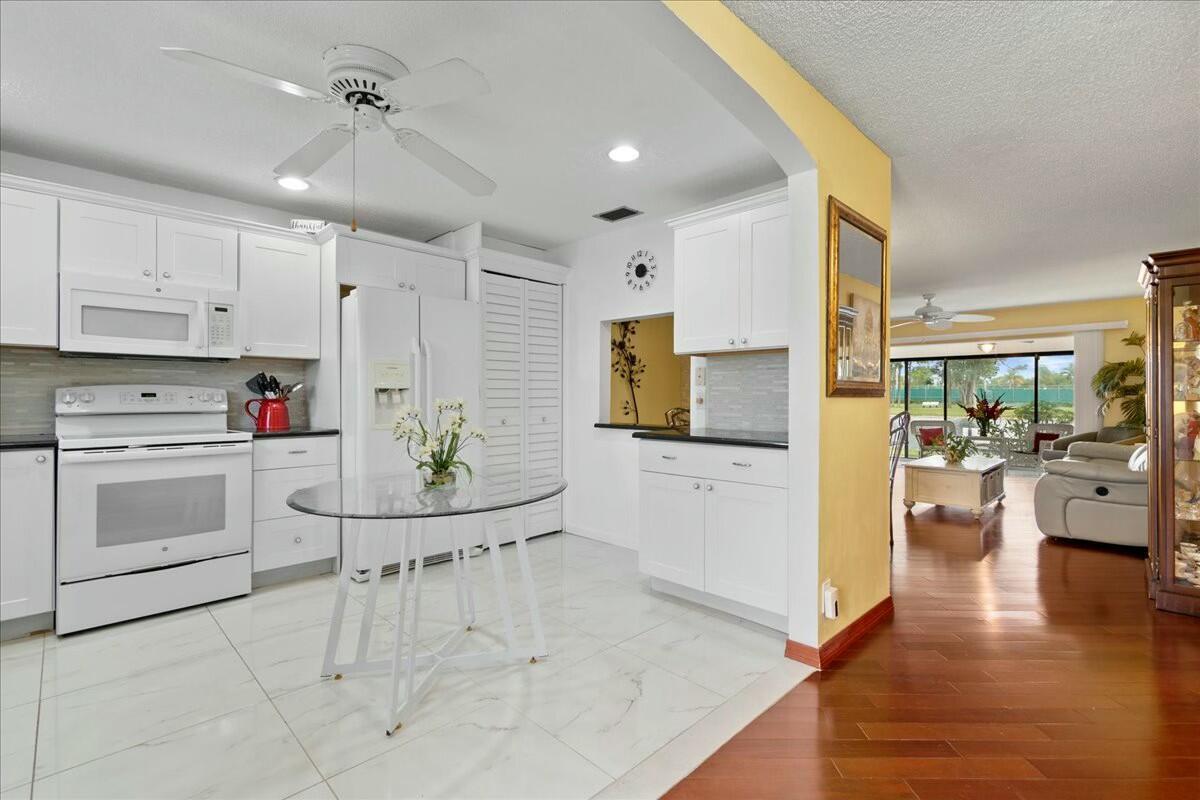 A kitchen with white cabinets, a glass table, and tile flooring opens to a living area — 603 Laconia Circle, Lake Worth FL 33467, LAKE WORTH, FL
