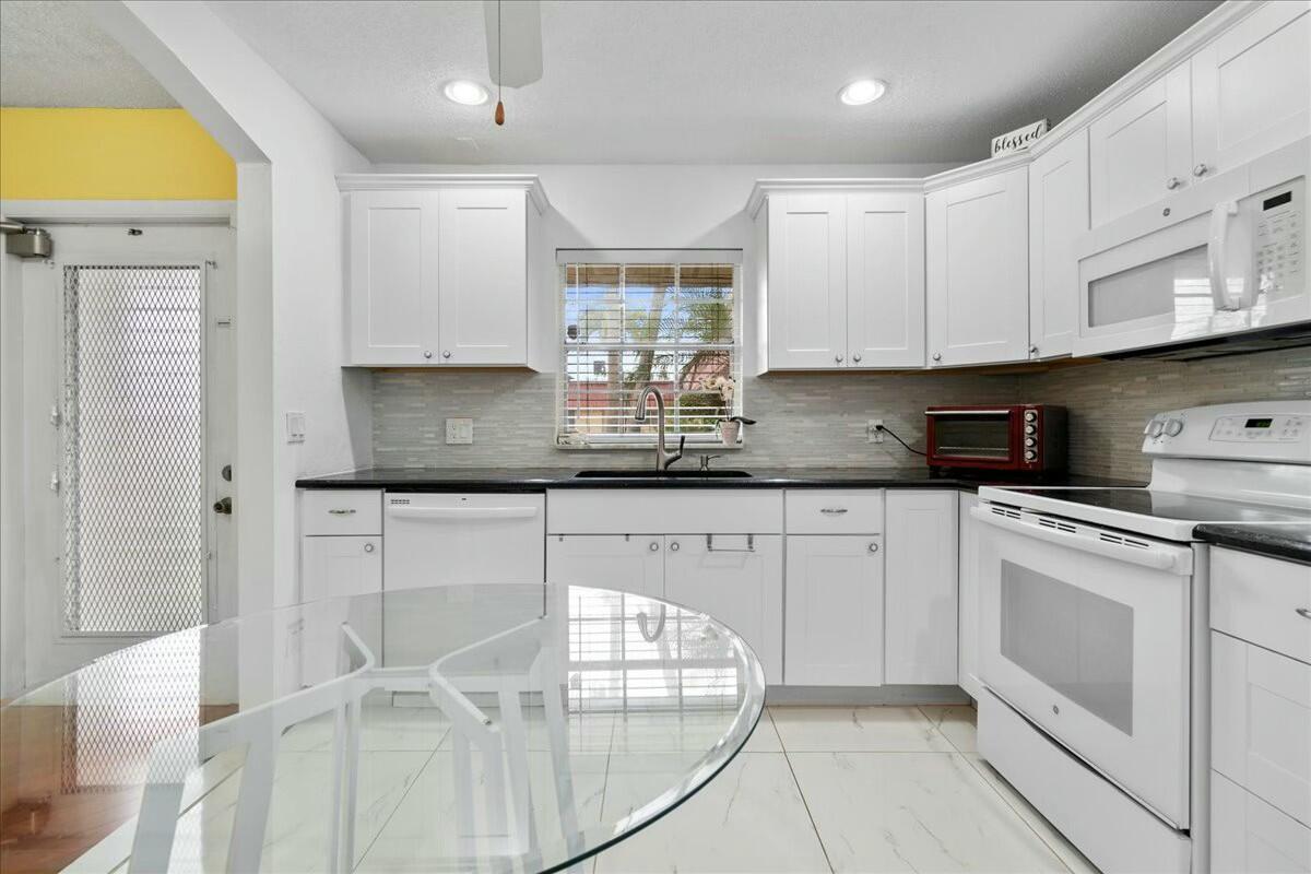 A bright kitchen features white cabinets, black countertops, a glass table, and a tiled floor — 603 Laconia Circle, Lake Worth FL 33467, LAKE WORTH, FL