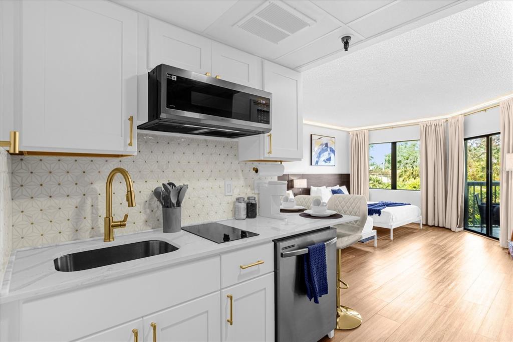 A modern kitchen with white cabinets and gold hardware overlooks a bedroom with a balcony — 6165 CARRIER DRIVE UNIT 3207, ORLANDO, FL