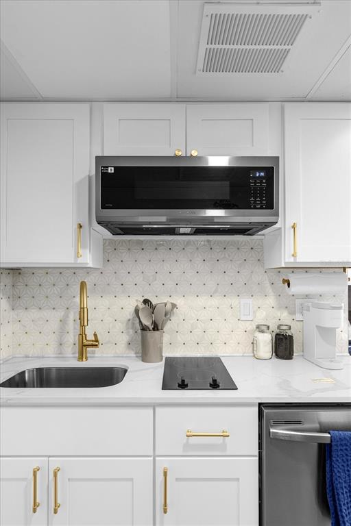 A kitchen features white cabinets, gold hardware, a patterned backsplash, and stainless steel appliances — 6165 CARRIER DRIVE UNIT 3207, ORLANDO, FL