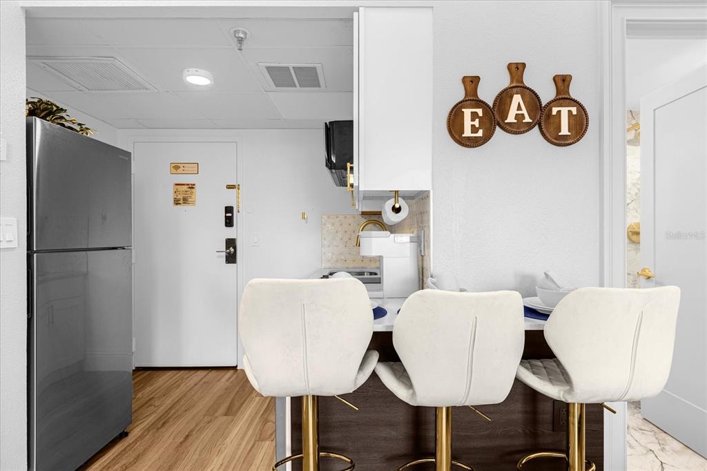 A kitchen features a breakfast bar with three white stools and "EAT" wall decor — 6165 CARRIER DRIVE UNIT 3207, ORLANDO, FL