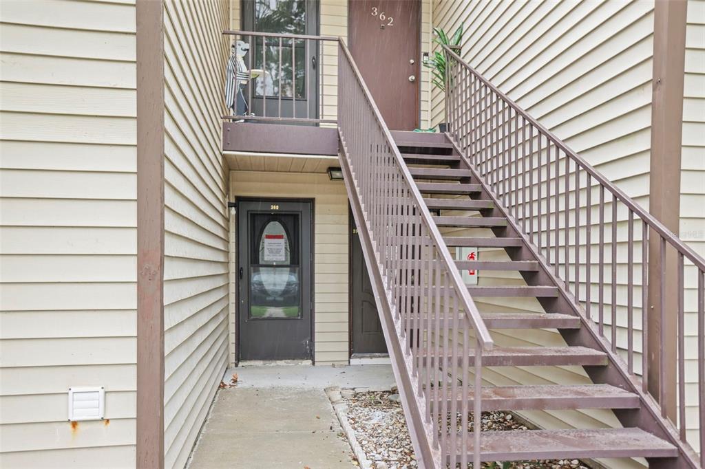 An exterior view shows a ground-level door, an upper-level door, and a metal staircase — 358 MOORINGS COVE DRIVE UNIT 4B, TARPON SPRINGS, FL