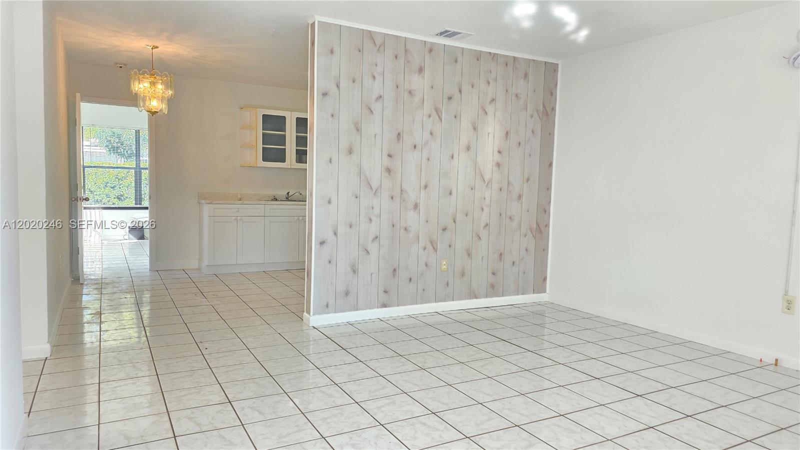A room with white tile floors features a wood-paneled accent wall and an adjacent kitchen — 525 NE 132nd Ter # 527, North Miami FL 33161, NORTH MIAMI, FL