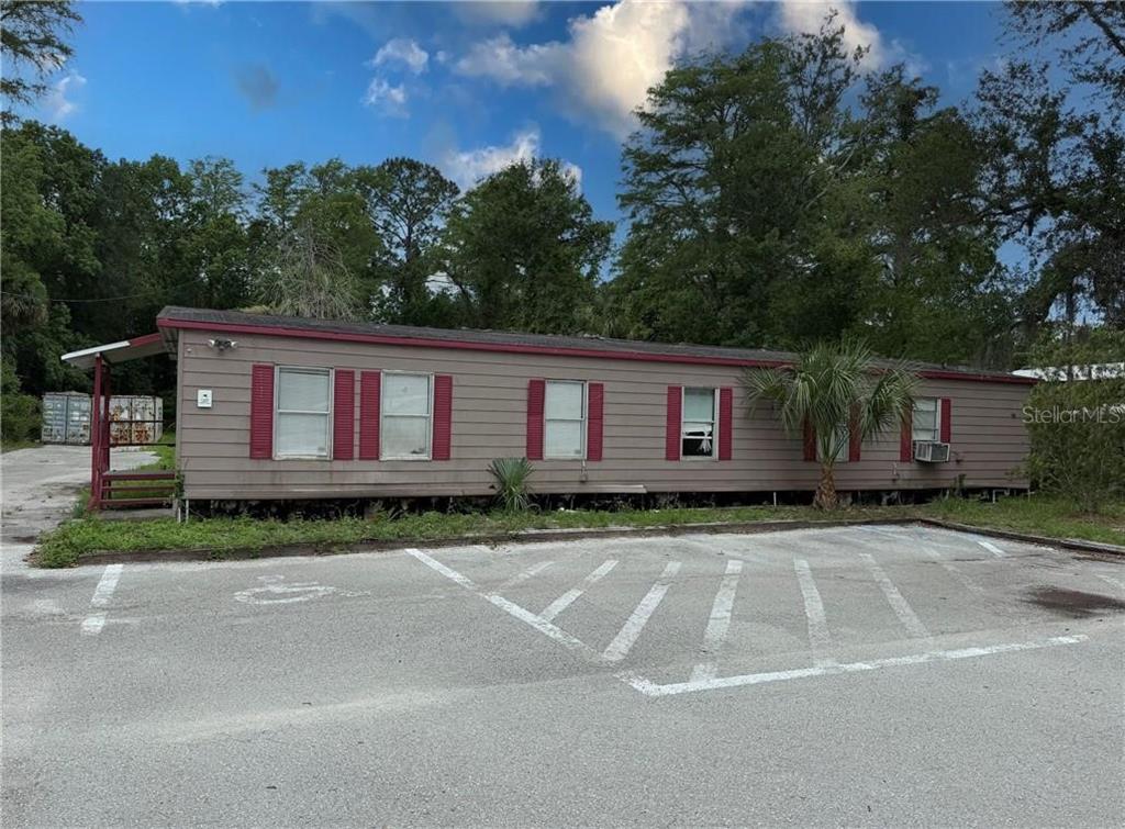 A single-story manufactured home with brown siding and red shutters sits behind a parking lot — 8144 W GROVER CLEVELAND BOULEVARD, HOMOSASSA, FL