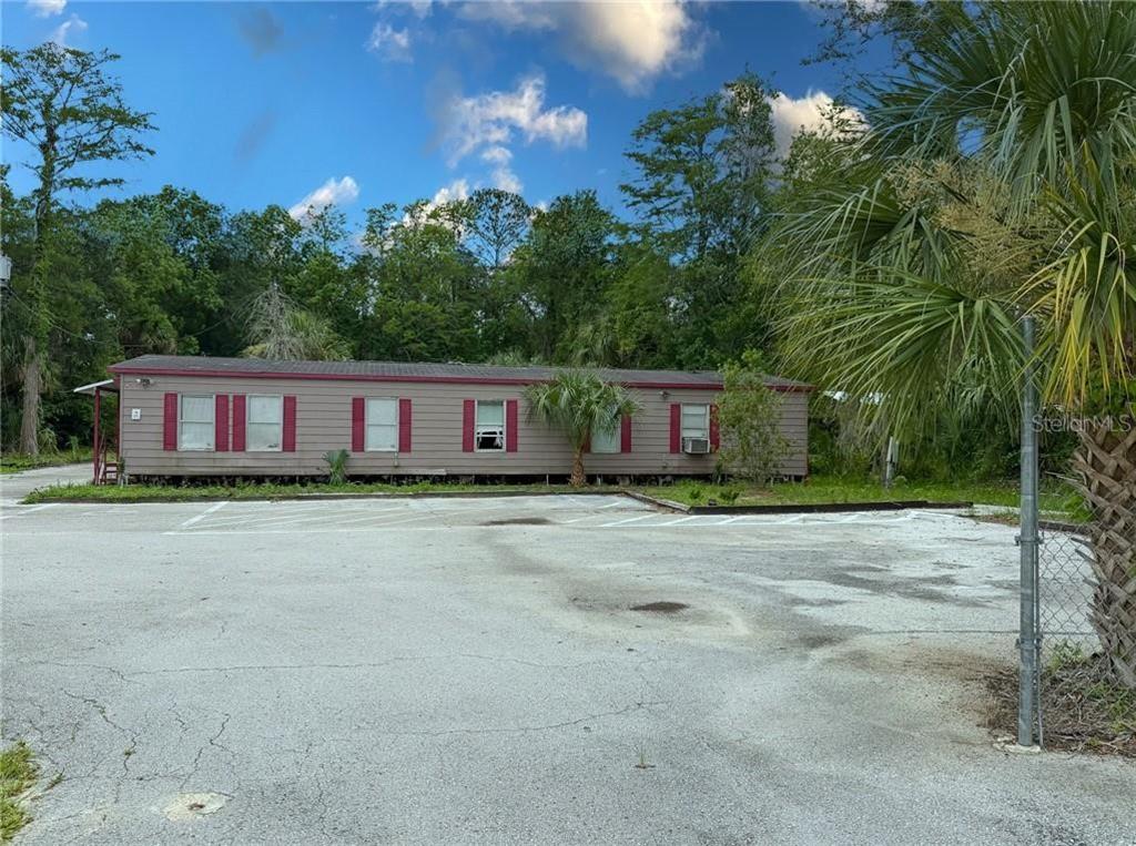 A long, single-story manufactured home sits behind a paved parking lot with a chain-link fence — 8144 W GROVER CLEVELAND BOULEVARD, HOMOSASSA, FL