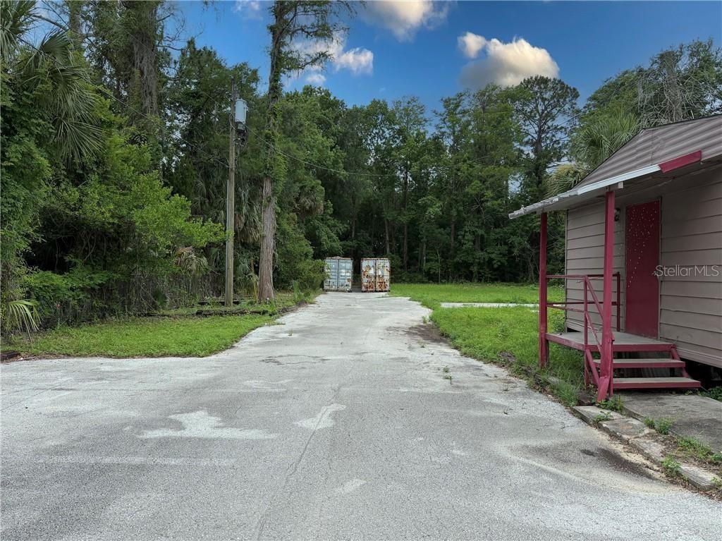 A paved driveway leads toward two shipping containers parked in front of a wooded area — 8144 W GROVER CLEVELAND BOULEVARD, HOMOSASSA, FL