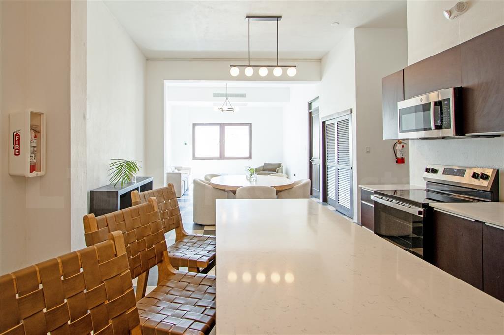 A modern kitchen with a white island and woven chairs overlooks a dining and living area — 254-256 SAN FRANCISCO STREET UNIT 203, SAN JUAN, PR