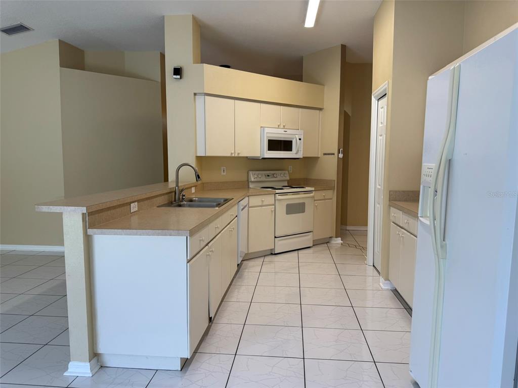 A kitchen features white cabinets, light countertops, white appliances, and tiled flooring — 4707 RAMSHEAD DRIVE, VALRICO, FL