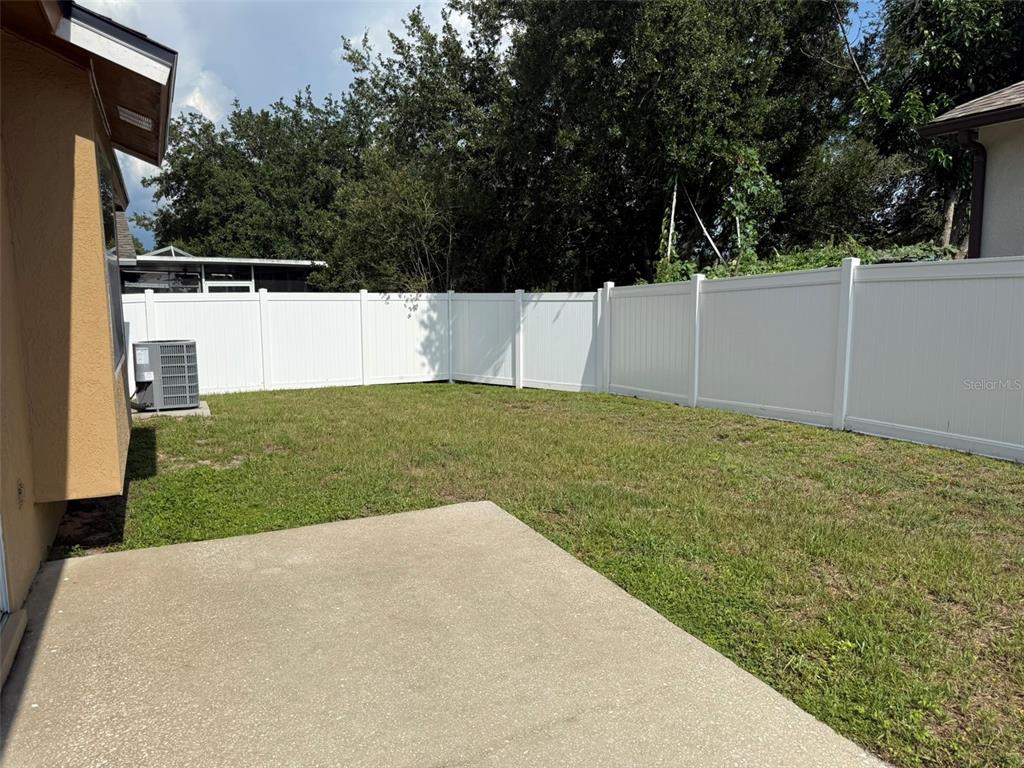 A concrete patio sits in a grassy backyard enclosed by a white vinyl privacy fence — 4707 RAMSHEAD DRIVE, VALRICO, FL