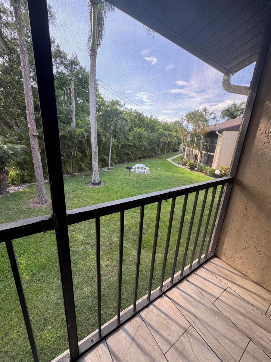 A screened-in balcony overlooks a grassy courtyard with palm trees and a neighboring building — 435 Pine Glen Lane # 2, FL 33463, FL