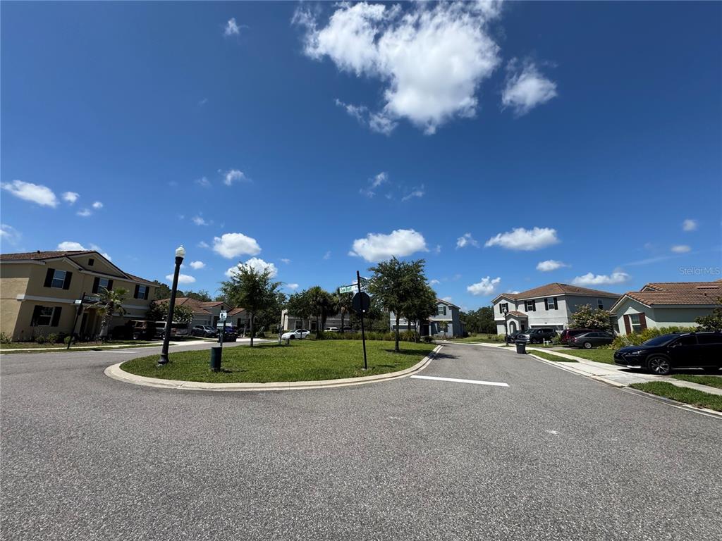 A residential street intersection features a grassy island, street signs, and suburban houses — 1512 OAK MARSH LOOP, DAVENPORT, FL