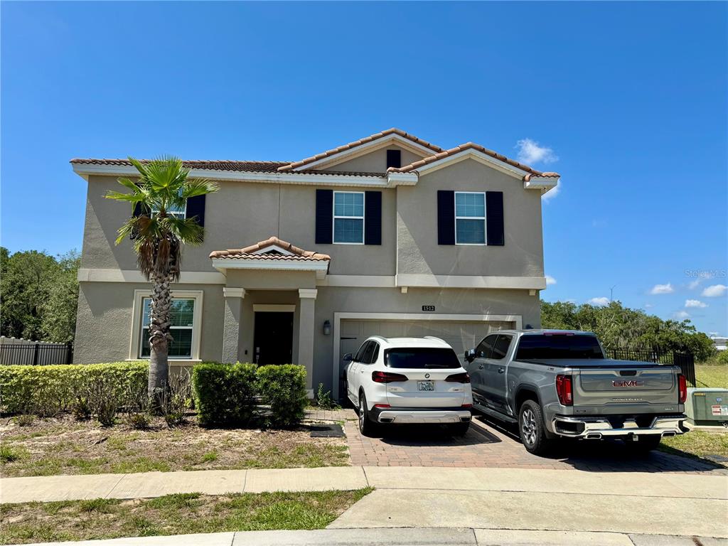 A two-story house with a beige exterior, a two-car garage, and two vehicles parked outside — 1512 OAK MARSH LOOP, DAVENPORT, FL
