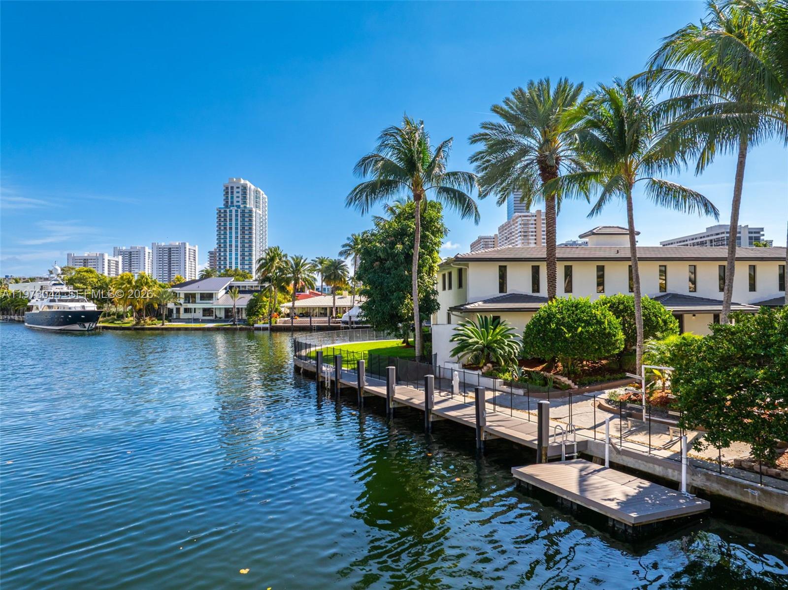 A waterfront property features a long wooden dock, palm trees, and a view of buildings — 501 Hibiscus Dr, Hallandale Beach FL 33009, HALLANDALE BEACH, FL