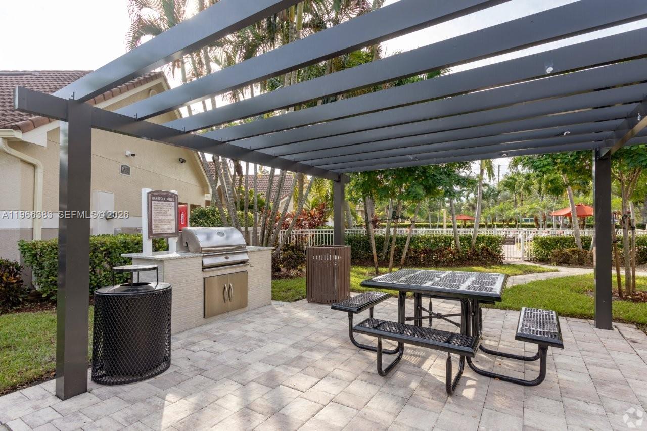 An outdoor patio features a metal pergola, a built-in grill, and a picnic table — NORTH LAUDERDALE, FL