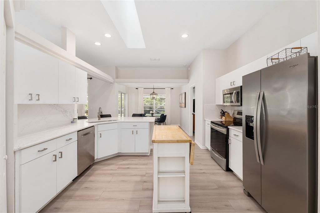 A modern kitchen features white cabinets, stainless steel appliances, a wood-topped island, and light flooring — 5248 NW 82ND COURT, OCALA, FL