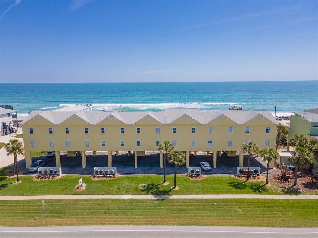 An elevated yellow multi-unit building stands along the coast with a view of the ocean — 6612 S ATLANTIC AVENUE UNIT 201, NEW SMYRNA BEACH, FL