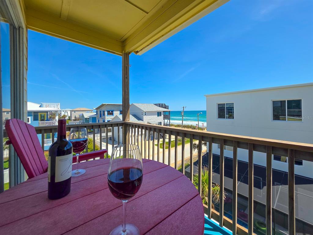 A balcony with a round table, wine, and chairs overlooks a beach and ocean view — 6612 S ATLANTIC AVENUE UNIT 201, NEW SMYRNA BEACH, FL