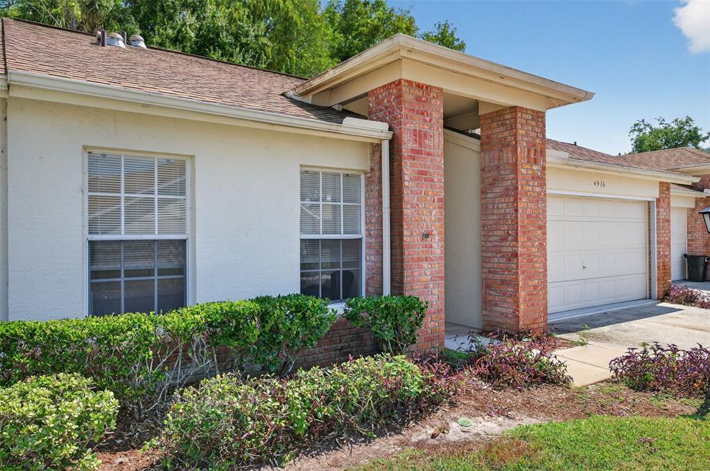 A single-story home exterior features a brick entryway, a garage, and a landscaped front yard — 4916 TROON LANE, NEW PORT RICHEY, FL